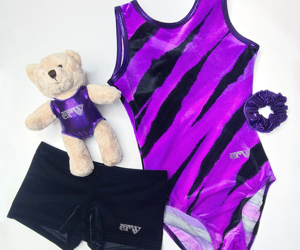 ERVY zauberhafte Geschenkeideen für Mädchen mit einen Samt Turnanzug mit Print in lila-schwarz und passender schwarzer Samt Hose, mit Teddybär mit schimmerndem violettem Turnanzug und Haargummi.